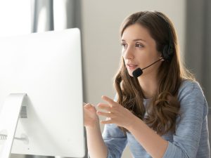 woman in headphones with microphone consulting client on phone in customer support service, looking at computer screen close up
